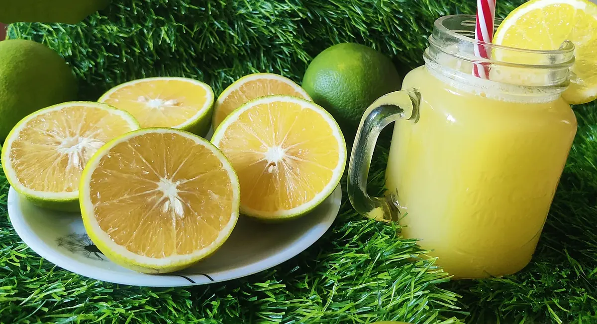 Halved sweet mosambi on a plate next to a glass of fresh mosambi juice